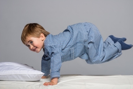 Energetic boy jumping into bed